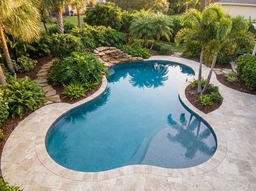 Rendering of freeform lagoon-style in-ground pool with soft curves, medium-blue pebble finish, travertine coping and deck, a small natural stone waterfall, tropical plantings and palms