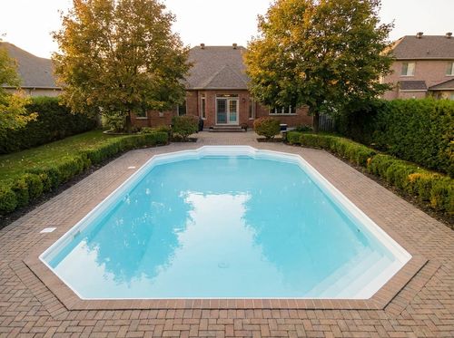 Rendering of Grecian-style in-ground pool with clipped corners, white plaster and light blue water, brick-paver deck, corner steps, traditional brick house, maple trees