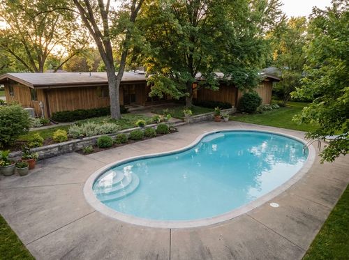 Rendering of classic kidney-shaped in-ground pool, white plaster with light blue water, brushed concrete deck, simple steps on the inside curve, mid-century ranch house, mature shade trees
