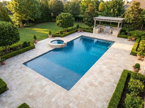 Rendering of large 20 by 40 foot rectangular pool with a tanning ledge, attached spa, and deep end, medium-blue pebble water, expansive travertine deck, outdoor kitchen, large estate backyard