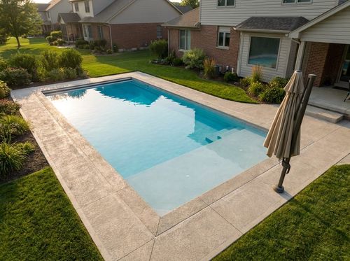 Rendering of 16 by 32 foot rectangular family pool with a tanning ledge and corner steps, light blue quartz water, broom-finished concrete deck, lawn, patio umbrella, suburban house