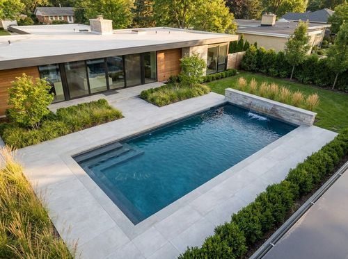 Rendering of modern rectangular pool with flush coping and large-format light gray porcelain pavers, dark finish with deep blue water, full-width steps, a single sheer descent water feature on a low wall, flat-roof contemporary house, minimal planting