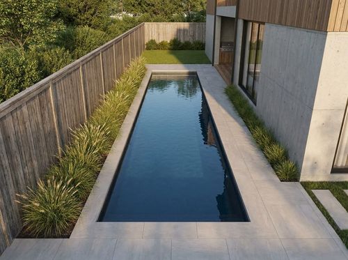 Rendering of long narrow 10 by 36 foot pool in a side yard between a modern house and a wood fence, dark finish with deep blue water, porcelain paver deck, linear planting of grasses