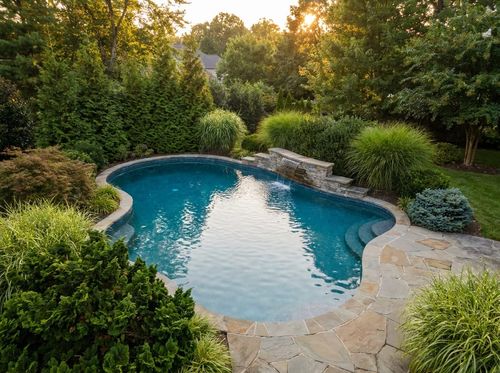Rendering of freeform pool with a modest stacked-stone waterfall about four feet wide on the far edge, pebble finish with blue water, flagstone deck, evergreen and ornamental grass planting, soft evening light