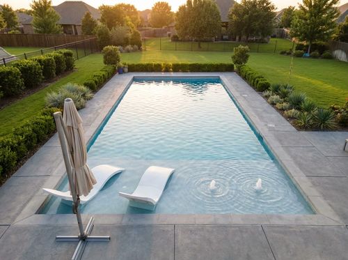 Rendering of rectangular pool with a wide tanning ledge in the foreground holding two in-water loungers and an umbrella, two small bubblers on the ledge, light blue quartz water, concrete paver deck, suburban backyard