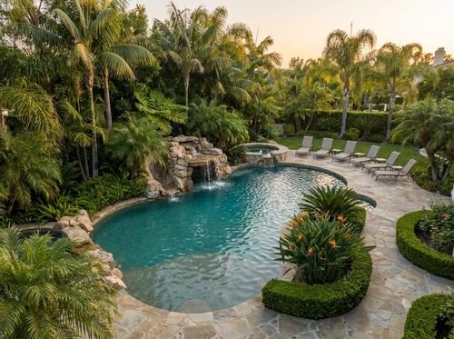 Rendering of tropical freeform pool with a natural rock waterfall and grotto, pebble finish with blue-green water, flagstone deck, dense palms, bird of paradise, ferns, warm sunlight